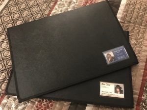 Two black portfolios with business card slots in the front. Business cards for author Mae Clair in slots